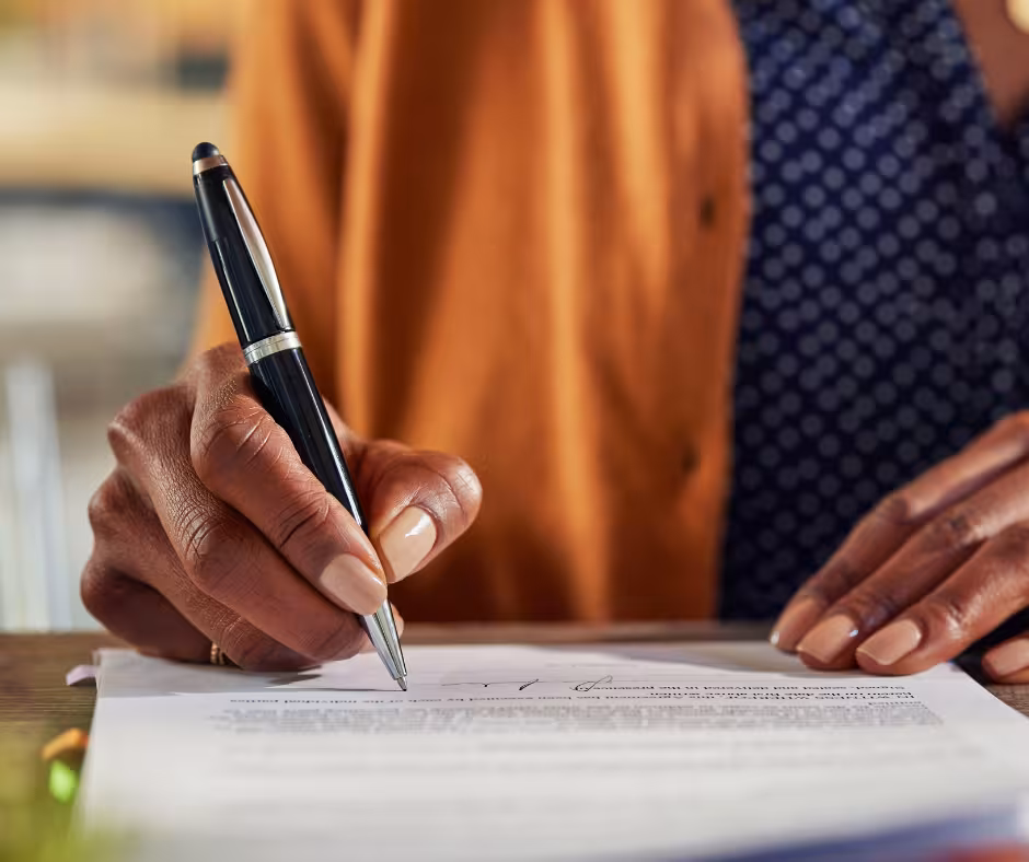A woman, pen in hand, writing on a paper document